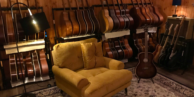 Showroom mit handverlesenen Akustikgitarren in Wandregalen und gemütlichem Sessel – 12Fret Guitars, Deutschland